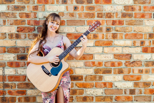 Happy female musician with guitar against brick wall