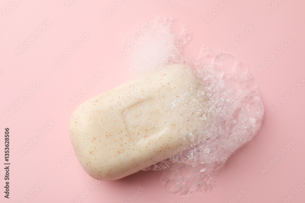 Fototapeta premium Soap bar with foam on light pink background, top view