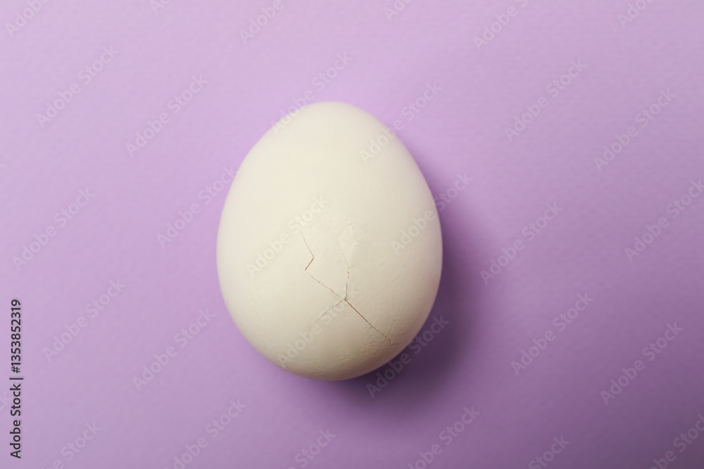 Fototapeta premium One egg with cracked shell on violet background, top view