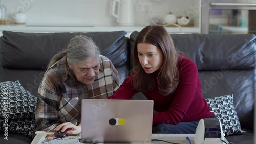 A woman patiently guides her elderly mother in managing their online store using a laptop, working together from the comfort of their home.