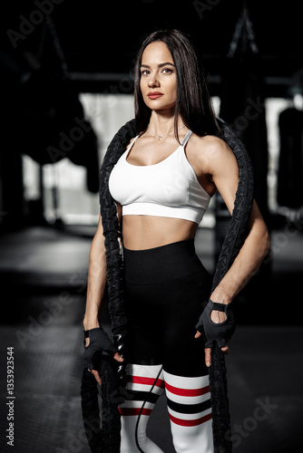 Portrait of fit muscular woman fitness trainer posing with battle ropes at the gym