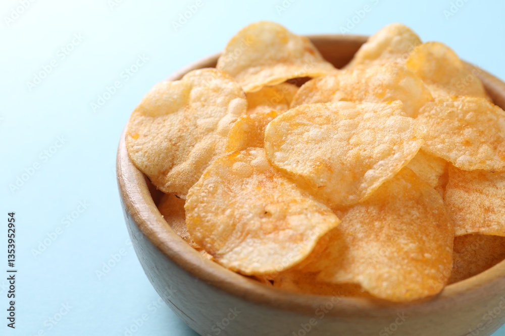 Tasty potato chips in bowl on light blue background, closeup Tasty potato chips in bowl on light blue background, closeup