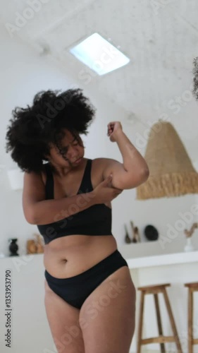 Vertical screen, beautiful plus size african american woman in black underwear assessing her body fat, pinching her abdomen and arm, concerned about her appearance and weight gain