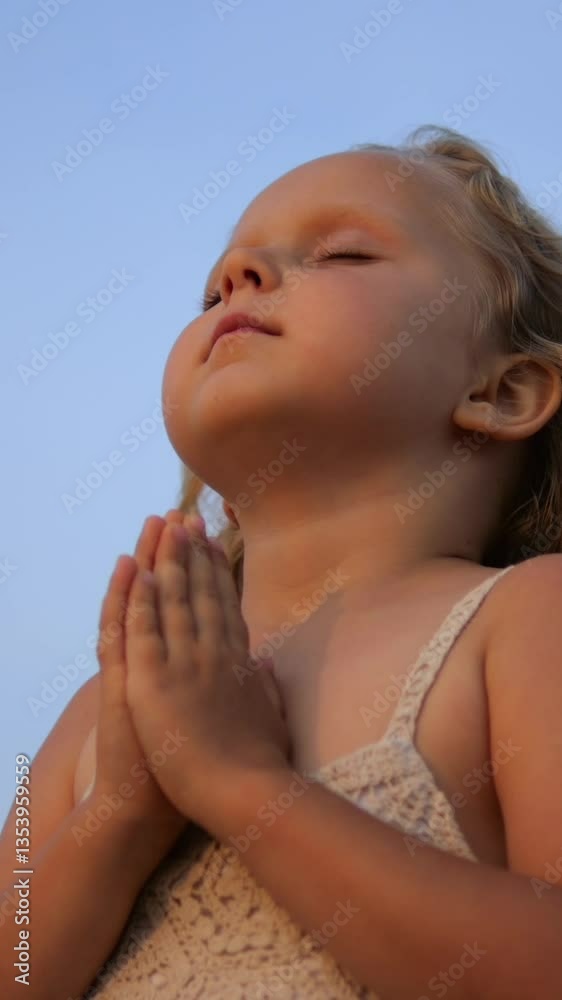 Vertical screen, blonde girl praying, joining hands with closed eyes, standing against bright blue sky, expressing deep spiritual connection and inner peace during golden hour sunlight Vertical screen, blonde girl praying, joining hands with closed eyes, standing against bright blue sky, expressing deep spiritual connection and inner peace during golden hour sunlight