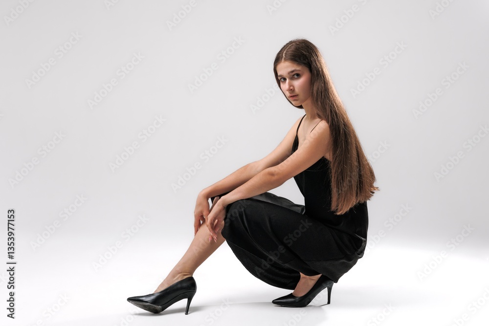 Young model poses gracefully in black dress and high heels against plain background Young model poses gracefully in black dress and high heels against plain background