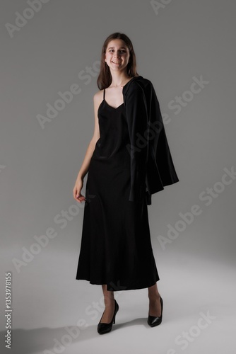 Model poses in elegant black dress with blazer in a studio setting during a fashion shoot