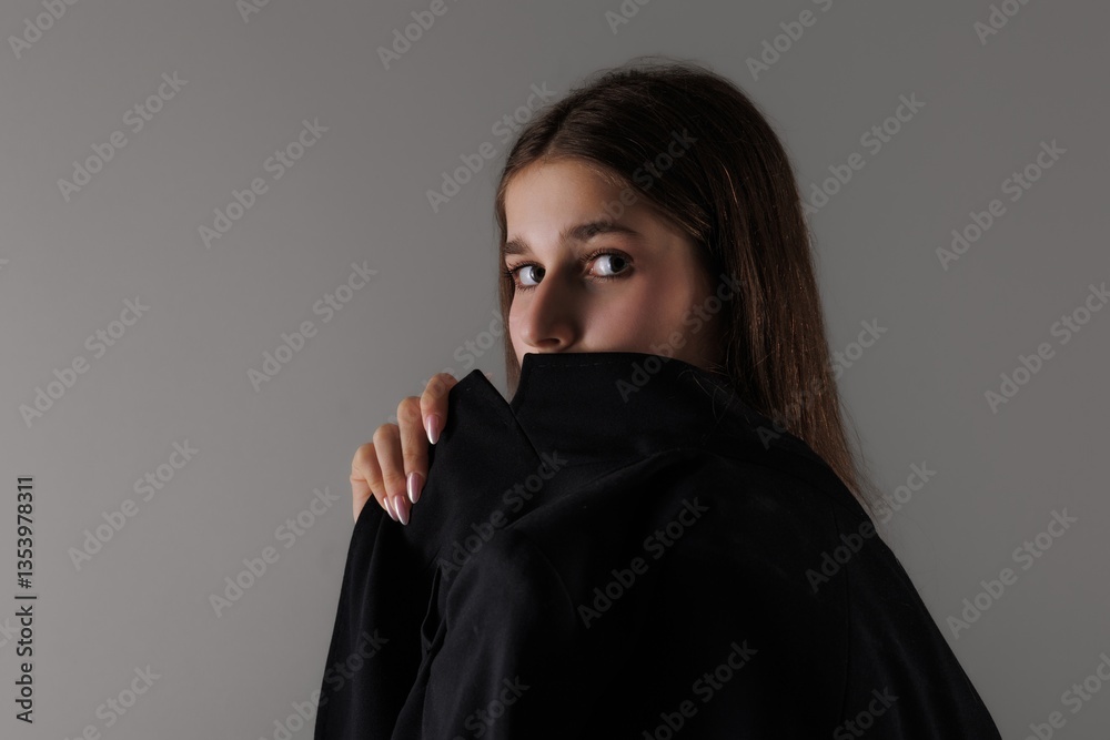 Fototapeta premium Young woman in black oversized hoodie poses against a neutral backdrop in an indoor setting