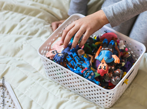 Various children's figures made from air plasticine in a box on a bed, a child examines