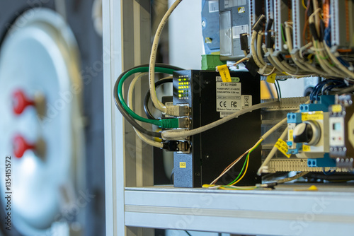 Close-up of industrial automation control system with Ethernet cables connected to network switch and PLC components inside electrical control cabinet
