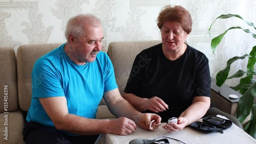 an elderly couple, a husband and wife, engaged in a thoughtful moment as they measure blood sugar levels using a home monitoring device.