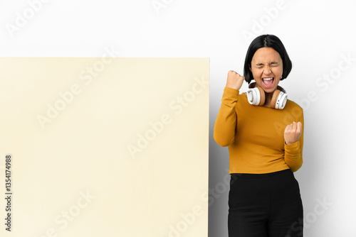 Young woman listening music with a big empty placard over isolated background celebrating a victory photo