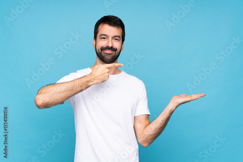Young man with beard  over isolated blue background holding copyspace imaginary on the palm to insert an ad