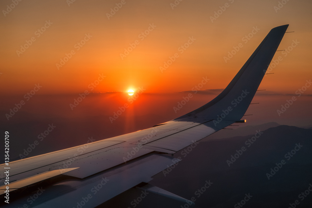 Beautiful view from airplane window on colorful orange sky with evening light and wing of plane