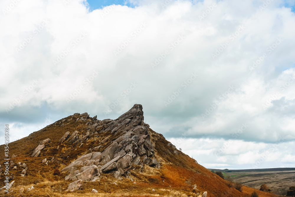 Fototapeta premium Rocky hill with cloud cover showcases natural beauty in a rural landscape during midday with vibrant grass and earthy tones
