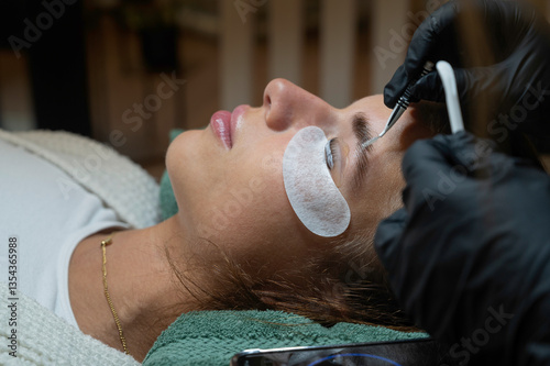 Beauty Close-up of a young woman having her eyebrows lash lifting enhanced with an eyelash lift by a beautician in a beauty salon. Shaping eye brow lash correction, color, curler, glue balm.