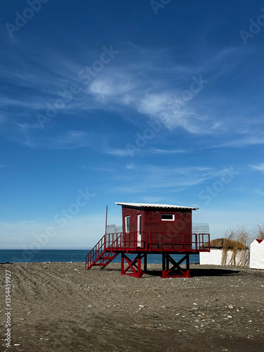 Obraz na płótnie Red Lifeguard Hut on Sandy Beach Under Blue Sky w salonie