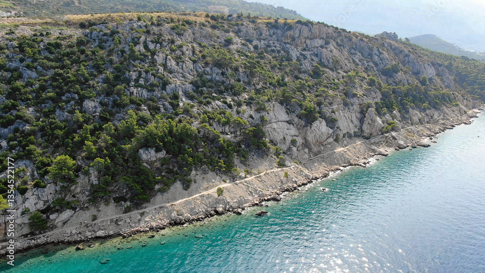 Obraz premium Scenic aerial view of a breathtaking coastal landscape with lush green mountains meeting the turquoise sea. A perfect destination for nature lovers and travel enthusiasts.