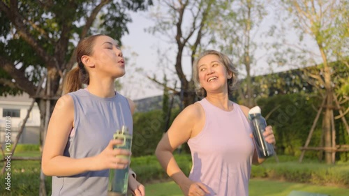 Young adult child workout outdoor public park run walk hold water bottle with mature middle age old mum. Love health care older mom asia elder people happy family protect aging fun joy city life sport