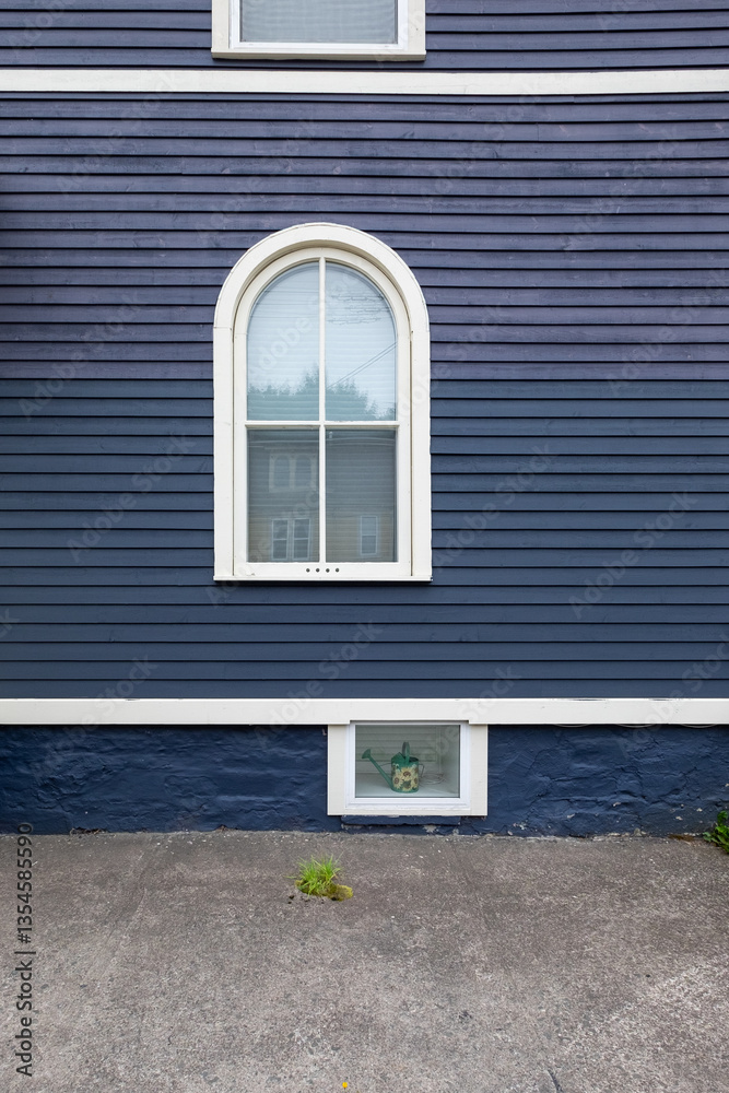 Fototapeta premium The exterior wooden wall of a vintage blue house with white painted trim. The building has three differently sized windows of various styles. The middle window is a half-round with four glass panes.