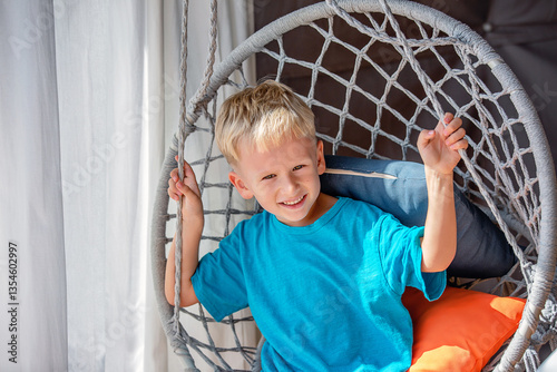 A portrait of a five-year-old blond-haired boy on a wicker swing.