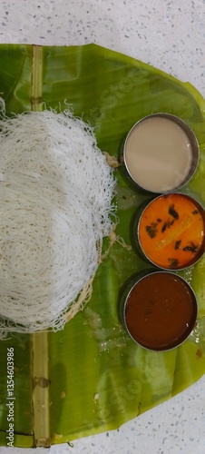  a traditional South Indian dish called Idiyappam,The idiyappam is neatly arranged in a circular pattern and is served on a fresh banana leaf, which enhances its presentation and flavor