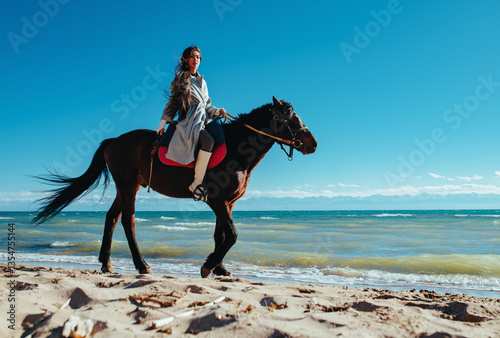Young asian woman ride on horse on lake shore on summer day