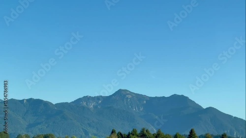 A stunning view of majestic mountains under a clear blue sky, captured while driving. The landscape feels calm and expansive, offering a peaceful moment on the road.