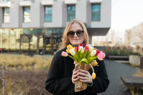 International Women's Day. Caucasian blonde happy woman smelling a bunch of spring flowers, which she is holding in her hands. Woman gets gift from husband. 