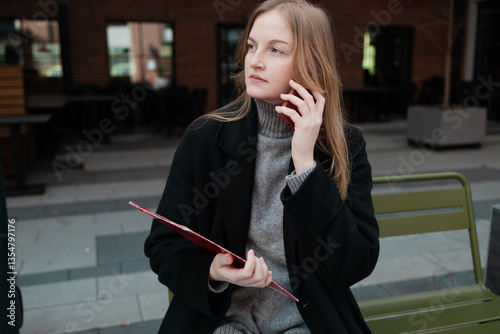 Obraz na płótnie Business woman with a red folder with documents talking on mobile phone outdoors, professional woman in suit sits on a bench near the business center w salonie
