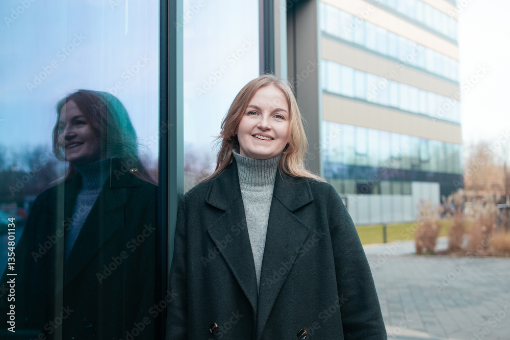 Blonde business lady girl In a stylish black coat standing near business center and looking at camera smiling. High quality photo