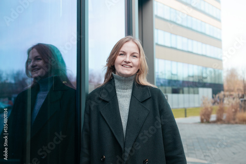 Obraz na płótnie Blonde business lady girl In a stylish black coat standing near business center and looking at camera smiling. High quality photo w salonie