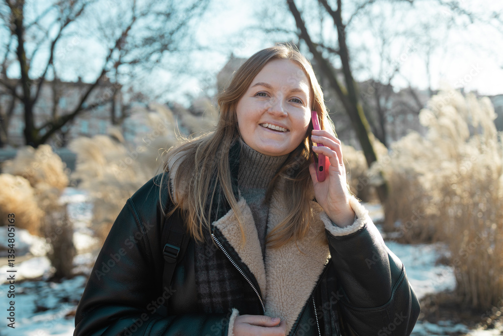 Happy smiling young woman portrait with phone enjoys winter weather at snowy winter park. High quality photo