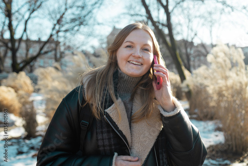 Obraz na płótnie Happy smiling young woman portrait with phone enjoys winter weather at snowy winter park. High quality photo w salonie