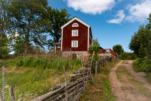 A wonderful old red farmhouse in eastern Småland, Sweden, with a path leading past the farm. A beautiful summer day with blue skies.