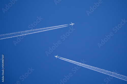 two white jets flying towards each other with long contrails in front of a blue sky