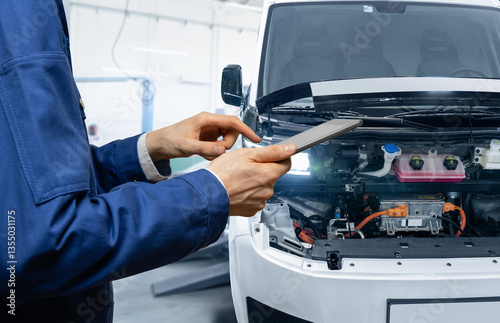 Serviceman with digital tablet next to electric van with open hood. Electric vehicles maintenance