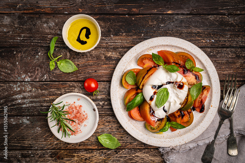 Caprese salad with burrata cheese, tomato, basil and balsamic vinegar arranged on white plate, on wooden background top view. High quality photo