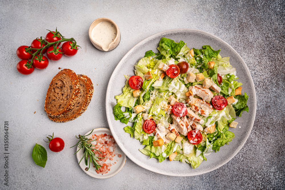 Fototapeta premium Fresh caesar salad with chicken breast, croutons, lettuce, parmesan cheese, sauce and tomatoes on gray background, top view. High quality photo
