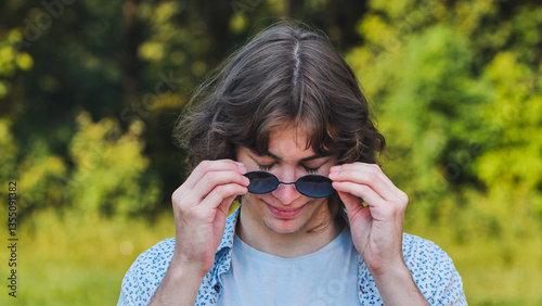 Bilde på lerret Cheerful young man playfully lowering his sunglasses and smiling in a sunny park