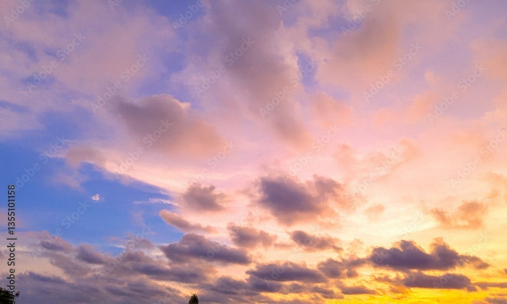Obraz premium Stunning sunrise sky with soft clouds in shades of blue, yellow, and white. A cinematic natural background perfect for summer scenes, nature designs, and atmospheric visuals.
