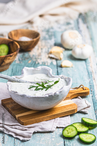 Greek tzatziki in a handmade white earthenware bowl with cucumber and garlic on a rustic wooden background