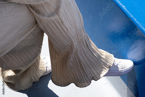 Legs of a young woman with light-colored, wide, pleated pants and white canvas shoes