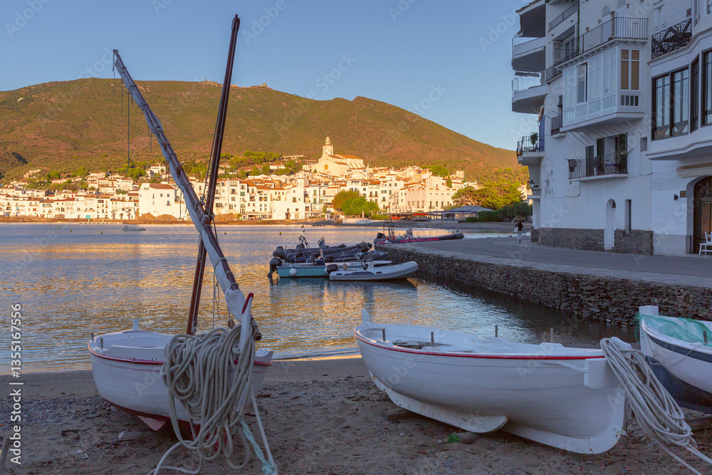 View of fishing boats in the bay of Cadaques in Catalonia, Spain with white buildings and church at sunset