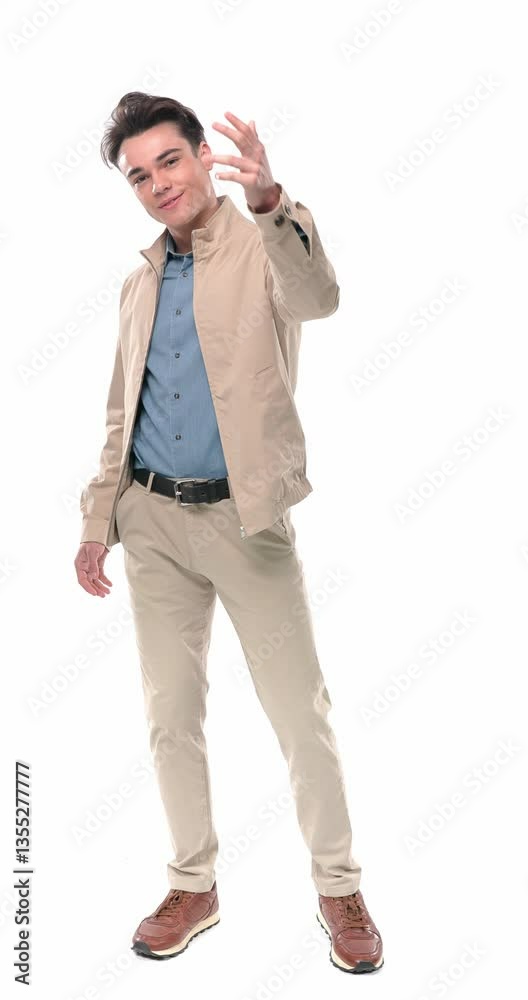 excited young man holding hand up and inviting to him, holding hands in pockets, smiling and being happy in front of white background excited young man holding hand up and inviting to him, holding hands in pockets, smiling and being happy in front of white background