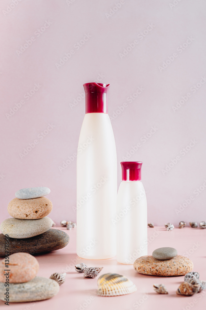 Pair of bottles with cosmetic products among stones and shells on pink vertical view