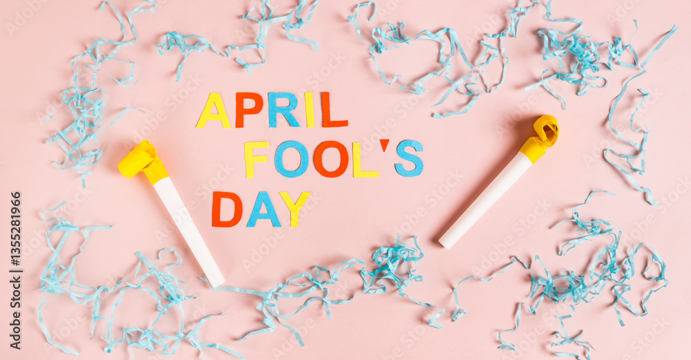 April Fools' Day from colored letters, whistles, balloons and paper on pink top view web banner