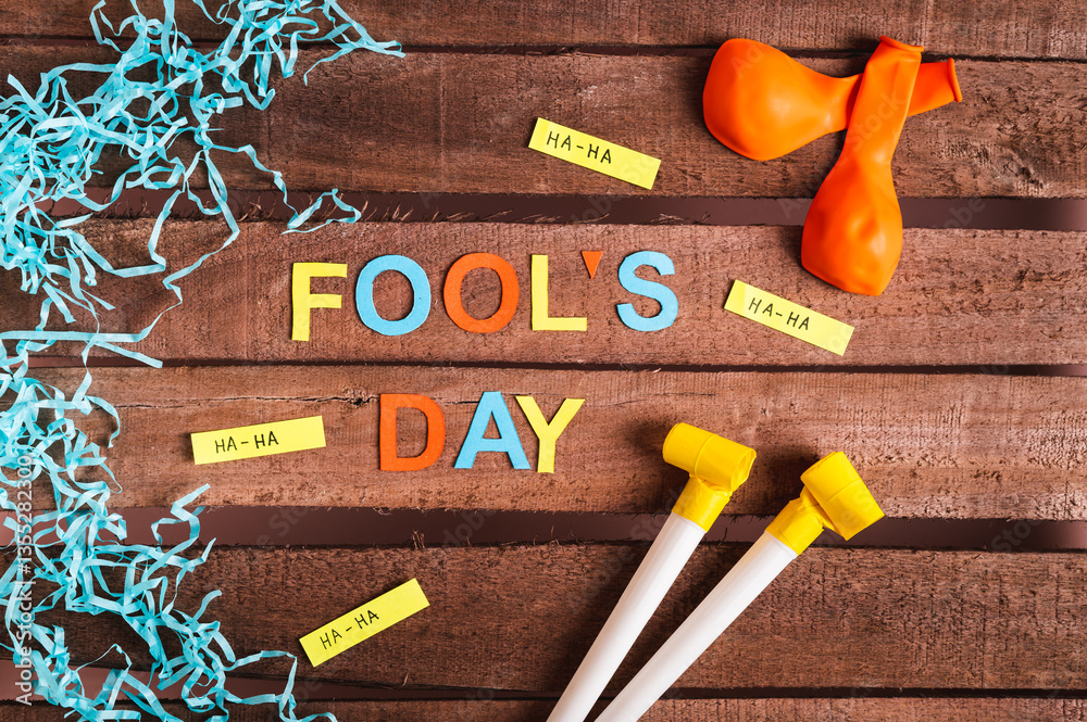 April Fools' Day from colored letters, funny notes, whistles and balloons on a wooden background