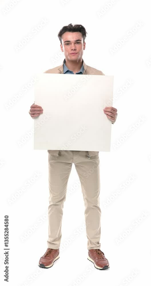 young casual guy in beige jacket holding empty board, looking down and smiling before walking away in front of white background young casual guy in beige jacket holding empty board, looking down and smiling before walking away in front of white background