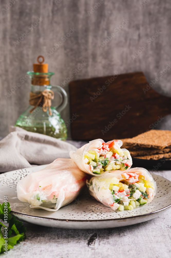 Spring rolls in rice paper with crab sticks, cucumber, greens and sauce on a plate on vertical view