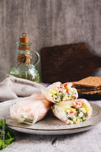 Spring rolls in rice paper with crab sticks, cucumber, greens and sauce on a plate on vertical view